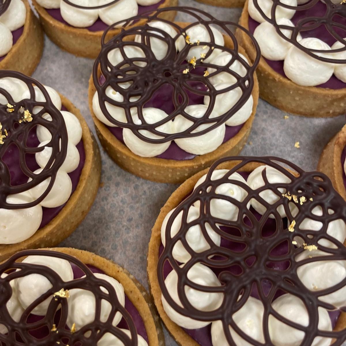 Mürbeteig-Tartelettes mit weinroter Kirschfüllung, weißem Rand aus Vanillemousse und Dekoration ausdunkler Kuvertüre mit Blattgold